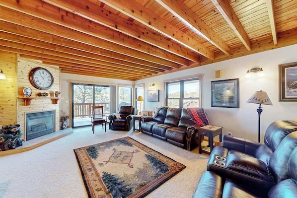 A spacious living room with a fireplace, leather sofas, a large rug, and wooden beams on the ceiling. - Buffalo Lodge - Ski-Area Cabin • Hot Tub & Views (Lead)