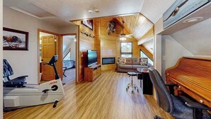 Ein geräumiger Wohnbereich mit Holzboden, einem Fernseher, einer Couch, einem Klavier und Trainingsgeräten.