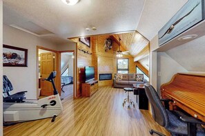 Ein geräumiger Wohnbereich mit Holzboden, einem Fernseher, einer Couch, einem Klavier und Trainingsgeräten.