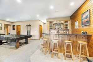 Ein Billardtisch mit Hockern, eine Bar mit Sitzgelegenheiten und eine Holzwand mit gerahmten Bildern.