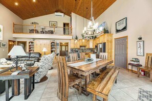 A spacious living area with a high ceiling, wooden furniture, and a dining table. - Boulder Canyon Lodge - Game Room Lodge w/ Hot Tub & Wet Bar (Sturgis)