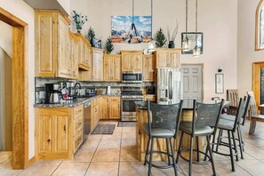 A kitchen with wooden cabinets, a central island with bar stools, a microwave, and a refrigerator. - Boulder Canyon Lodge - Game Room Lodge w/ Hot Tub & Wet Bar (Sturgis)