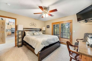 A bedroom with a bed, a desk, a chair, a ceiling fan, and a television.