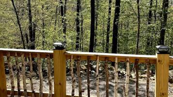 A wooden deck with a railing, overlooking a forested area.