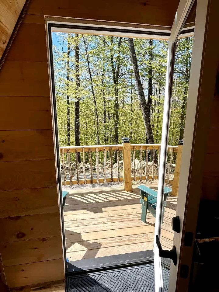 A wooden deck with a bench and a door leading to an outdoor area with trees.