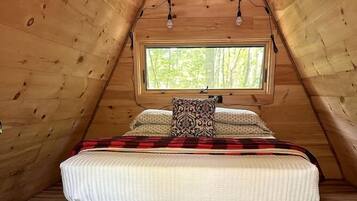 A cozy attic bedroom with a bed, a window, and a cowhide rug.