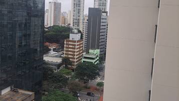 Um edifício alto com fachada de vidro moderna, rodeado por outros edifícios altos e uma rua com veículos.
