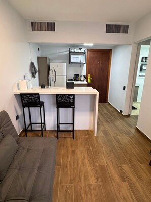 A compact living space with a kitchenette, a sofa, and a door leading to another room.