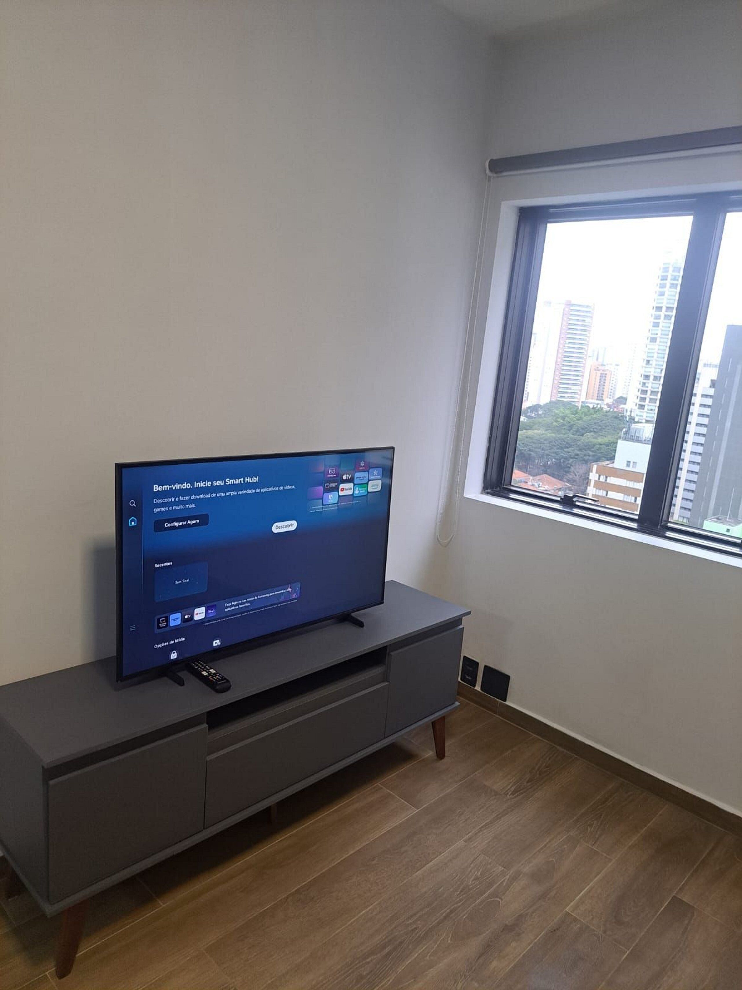 Uma televisão sobre um armário cinzento numa divisão com uma janela.