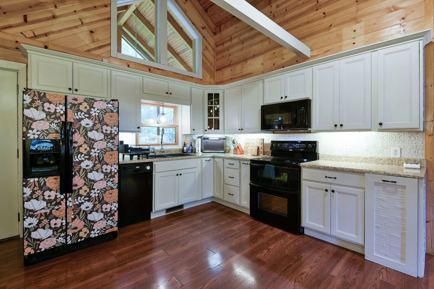 A kitchen with wooden flooring, white cabinets, a black refrigerator, a microwave, and a stove.