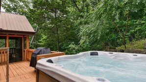 A hot tub on a wooden deck with a covered seating area and a small building in the background.