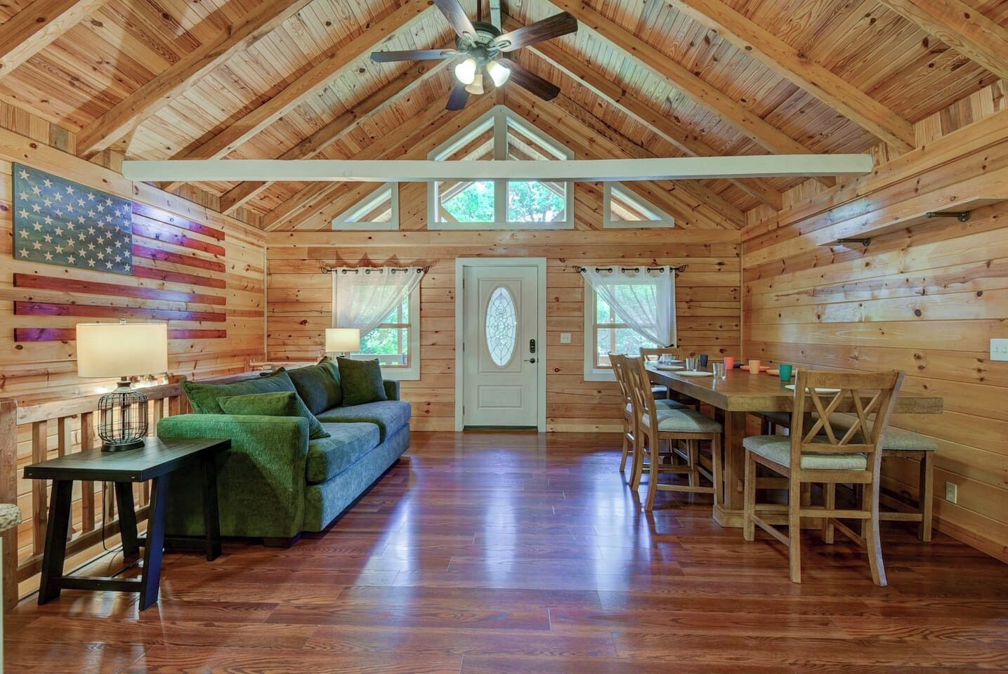 A log cabin interior with a dining area, a sofa, and a flag on the wall.