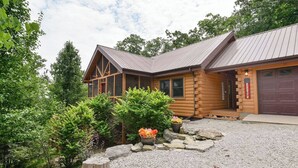 A log cabin with a metal roof, a garage, and a gravel driveway.