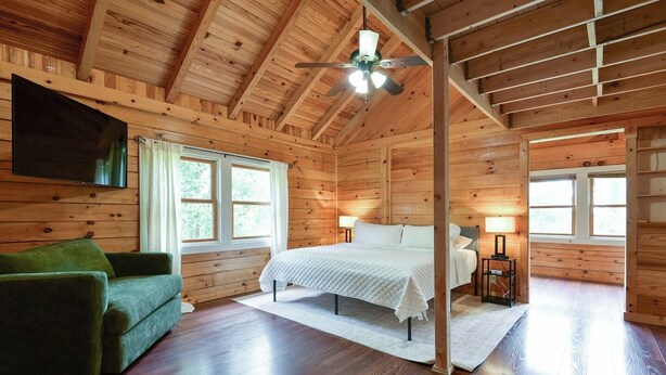 A wooden cabin interior with a bed, a green sofa, and a ceiling fan.