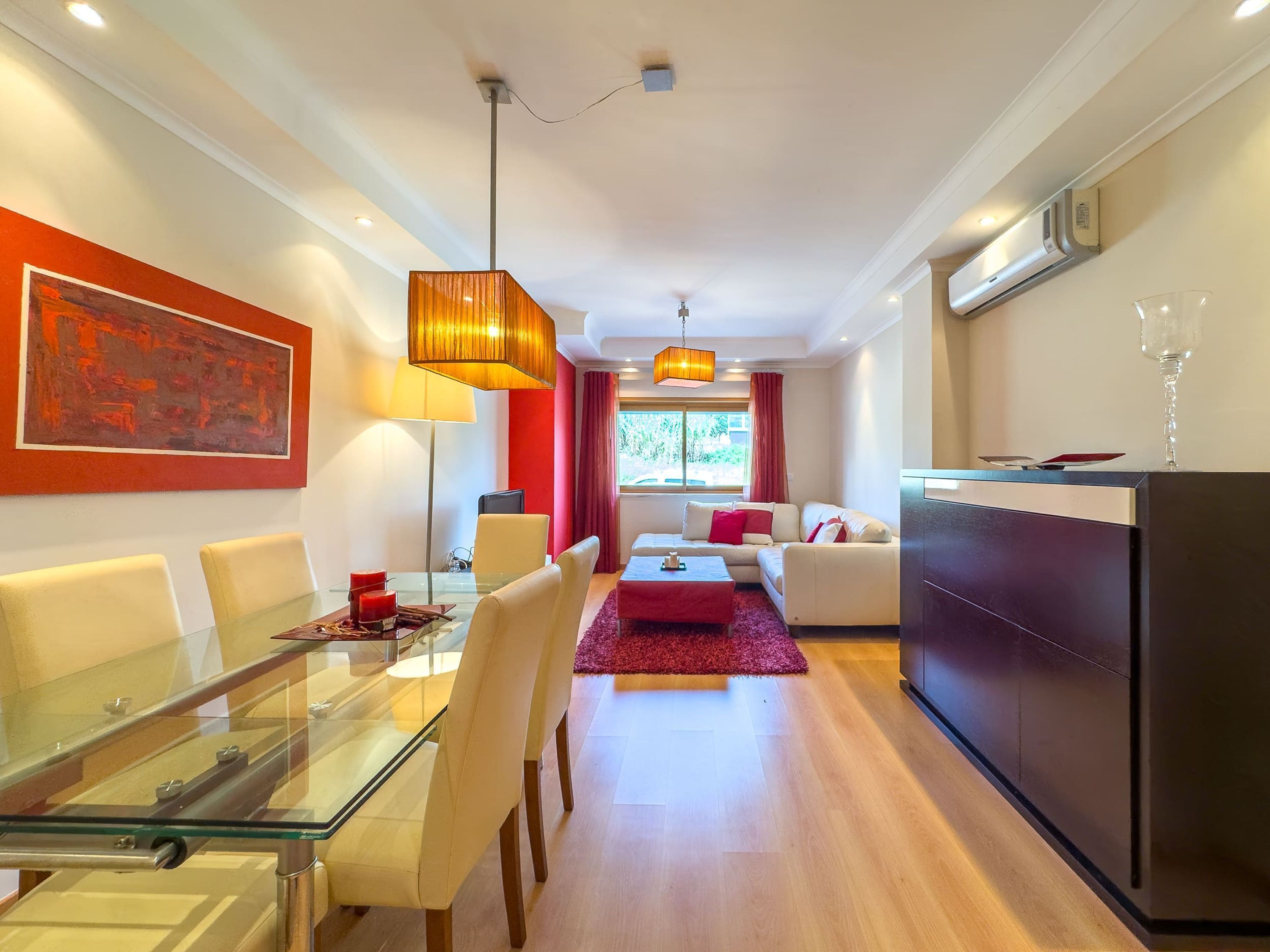A modern living room with a glass dining table, red accents, and a view to the outside.