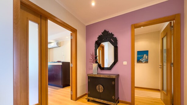 A hallway with wooden flooring, a dark console table with a mirror, and a painting on the wall. - Ref gio do Mar by Acasadascasas (Mafra)