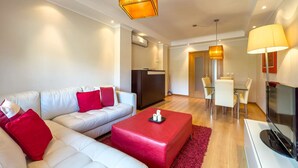 A modern living room with a sofa, red ottoman, and a TV. - Ref gio do Mar by Acasadascasas (Mafra)