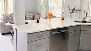 A modern kitchen with grey cabinets, a white countertop, and a built-in dishwasher. - Spacious Townhome near Disney (Davenport)