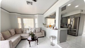A modern living room with a sectional sofa, a coffee table, and a dining area with a kitchen in the background. - Spacious Townhome near Disney (Davenport)