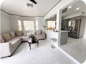 A modern living room with a sectional sofa, a coffee table, and a dining area with a kitchen in the background. - Spacious Townhome near Disney (Davenport)