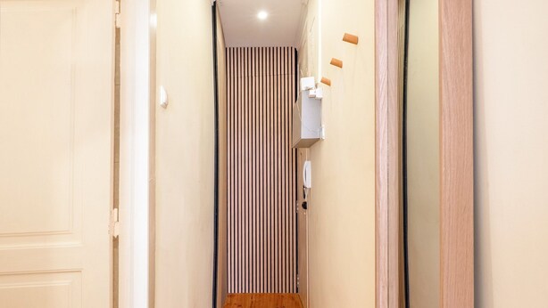 Un pasillo estrecho con suelo de madera, pared a rayas y una puerta a la izquierda.