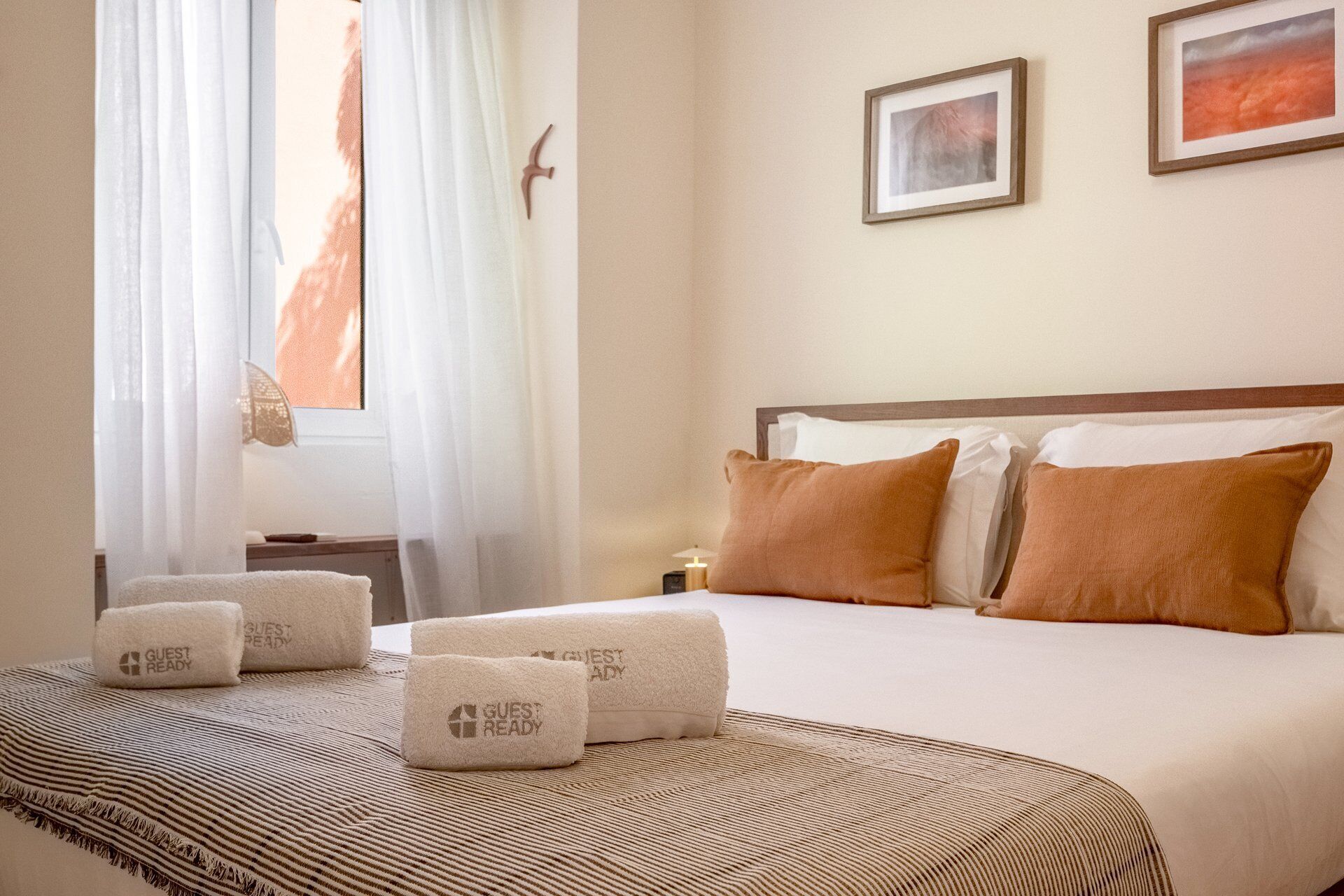 A hotel room with a bed, two pillows, a bedside table with a lamp, and a window with curtains.