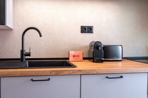 A modern kitchen with a black faucet, a coffee machine, a box labeled 'GUEST READY,' and a power outlet on the wall. - GuestReady - Stay in the Heart of Lisbon (Lisbon)