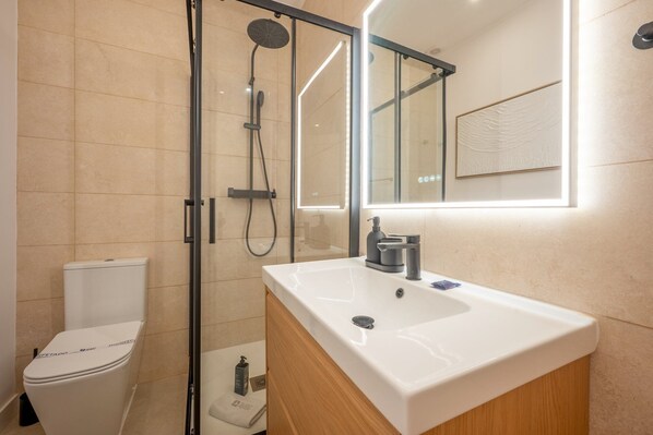 Une salle de bain moderne avec une douche à parois de verre, des toilettes blanches et un meuble-lavabo avec un évier et un miroir.