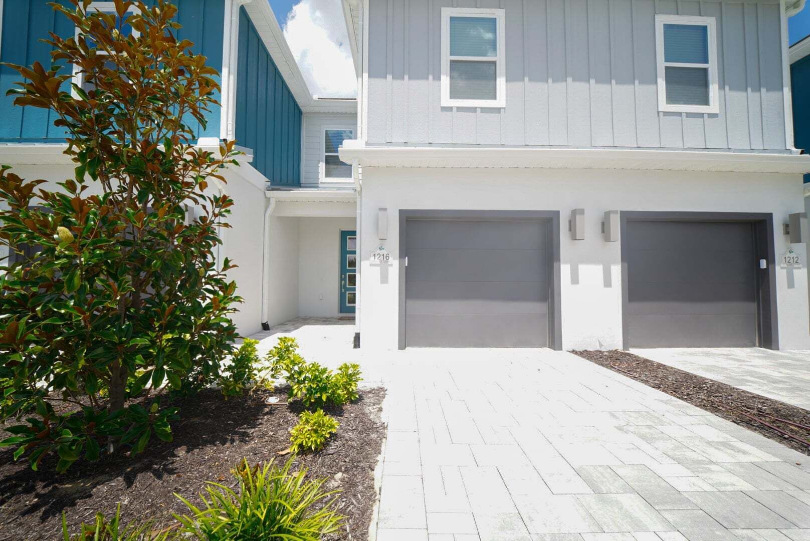A modern two-story residential building with a garage, a driveway, and a small garden area.