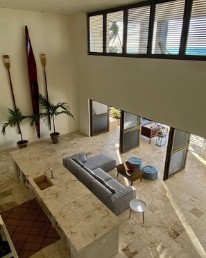 A modern interior with a large sofa, a kitchen area, and a view through a window.