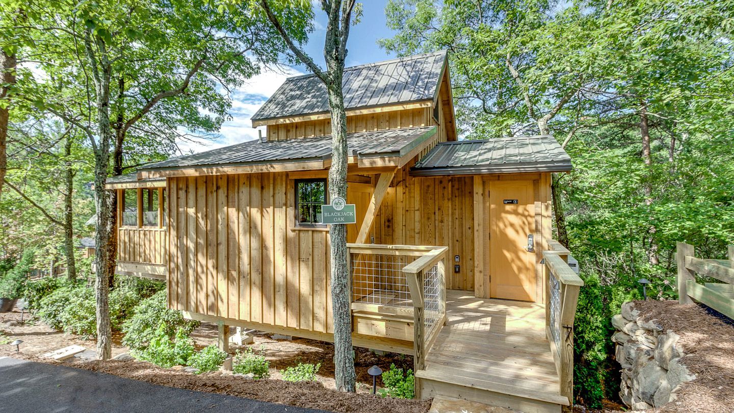Une cabane en bois avec un porche, entourée d’arbres.