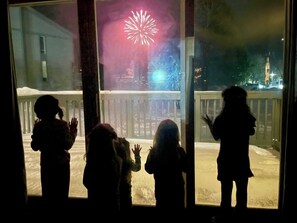 Blick durch ein Fenster, der Silhouetten von Menschen zeigt, die Feuerwerk beobachten.