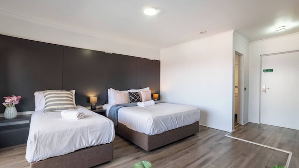 A modern hotel room with two beds, a dark accent wall, and a wooden floor. - Room-deluxe Twin Room - Sleeps 3 (Sydney)