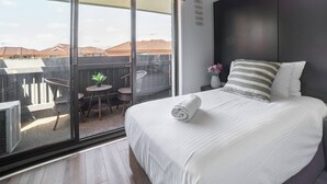 A bedroom with a large bed, a nightstand, a potted plant, and a view of the outside. - Room-deluxe Twin Room - Sleeps 3 (Sydney)