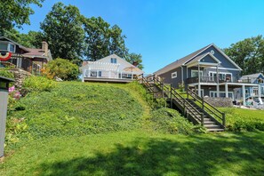 A residential area with houses, a grassy hill, and a wooden staircase leading to a porch. - Paddle & Play on Long Lake - Lakefront Retreat (Scotts)