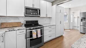 A modern kitchen with white cabinetry, a stainless steel stove, a microwave, and a refrigerator. - Paddle & Play on Long Lake - Lakefront Retreat (Scotts)