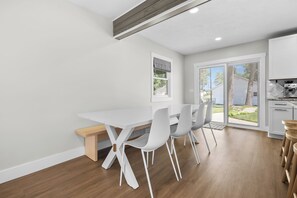 A modern kitchen with white cabinetry, a built-in oven, and a dining area with a white table and chairs. - Paddle & Play on Long Lake - Lakefront Retreat (Scotts)