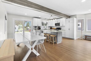 A modern kitchen with white cabinetry, a central island with stools, and a dining table. - Paddle & Play on Long Lake - Lakefront Retreat (Scotts)