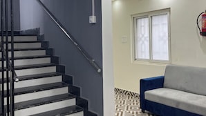 A staircase with black steps and a metal handrail, leading to a room with a patterned floor and a blue sofa.