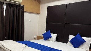 A hotel room with a bed, dark curtains, a wall-mounted air conditioner, and a headboard.