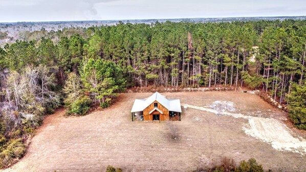 A single-story wooden cabin with a gabled roof, surrounded by a dense forest.