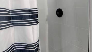 A shower area with a striped shower curtain, a handheld showerhead, and a tiled floor.