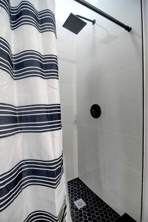 A shower area with a striped shower curtain, a handheld showerhead, and a tiled floor.