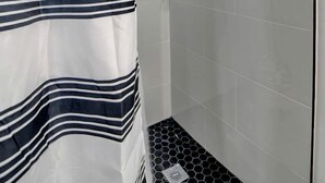 A shower area with a striped shower curtain, a handheld showerhead, and a tiled floor. - Luxury Vineyard Barn Retreat with Private Trails Near Nashville, Georgia (Nashville)