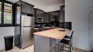 A modern kitchen with dark cabinetry, stainless steel appliances, a wooden island, and a black trash bin.