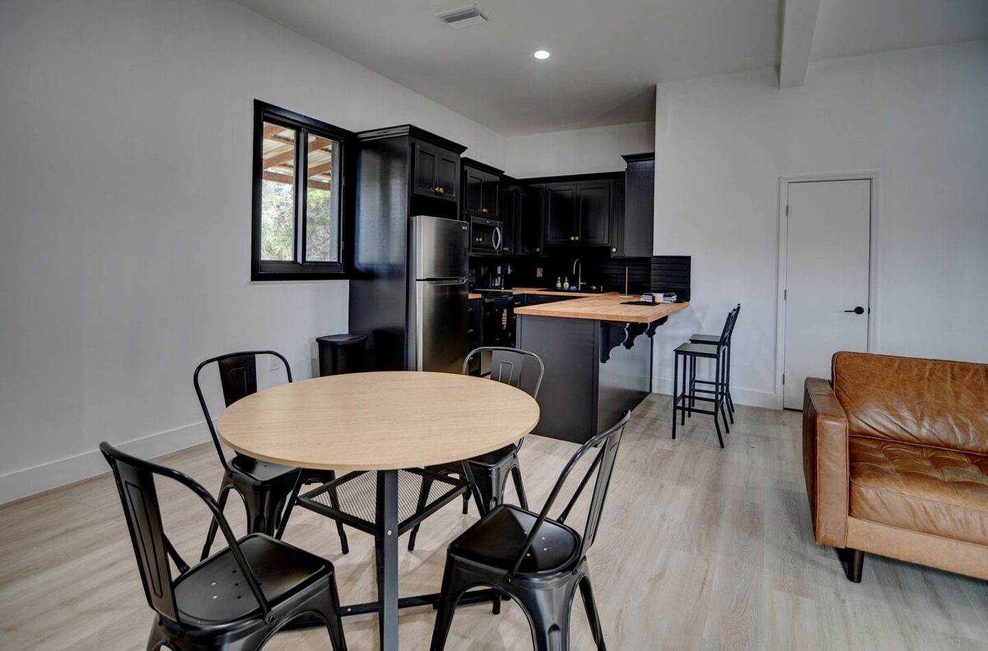 A modern kitchen with dark cabinetry, a stainless steel refrigerator, and a wooden island.