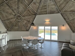 A spacious room with a high ceiling, a dining table with chairs, a sofa, and a view of a swimming pool through a glass door. - Modern 3-Bedroom Lakefront Home with Pool, Patio & Private Helipad in Clermont, Florida (Clermont)
