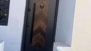 Una puerta moderna con mirilla y ojo de buey, en un edificio de fachada blanca y suelo de baldosas.