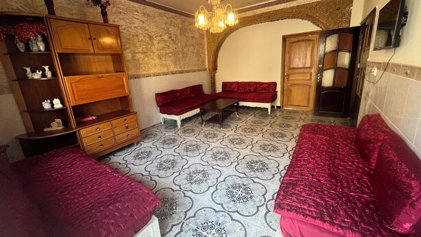 Una habitación con piso estampado, un mueble de madera, un banco y una puerta que da a otra habitación.
