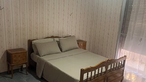 Un dormitorio con cama, una mesita de noche, suelo estampado y una ventana con cortina.